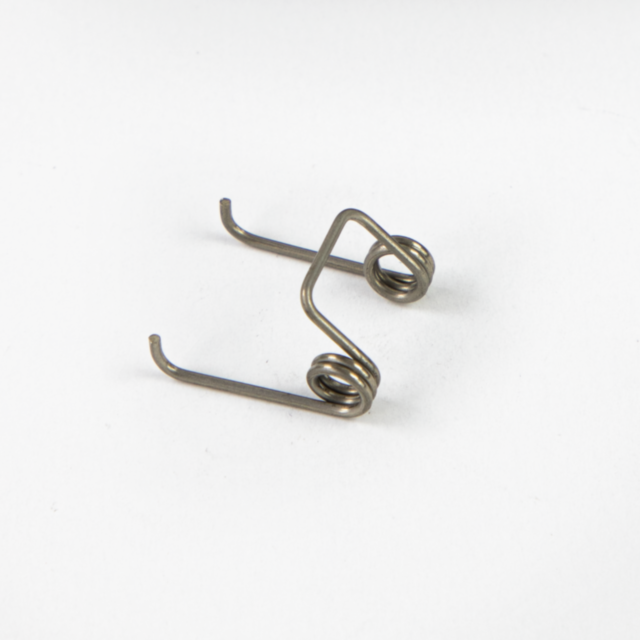 Close-up of the TRIGGER SPRING BREN 2, a small metal torsion spring, on a plain white background. The spring features two coils with extended arms ending in hooks, forming an angular shape.