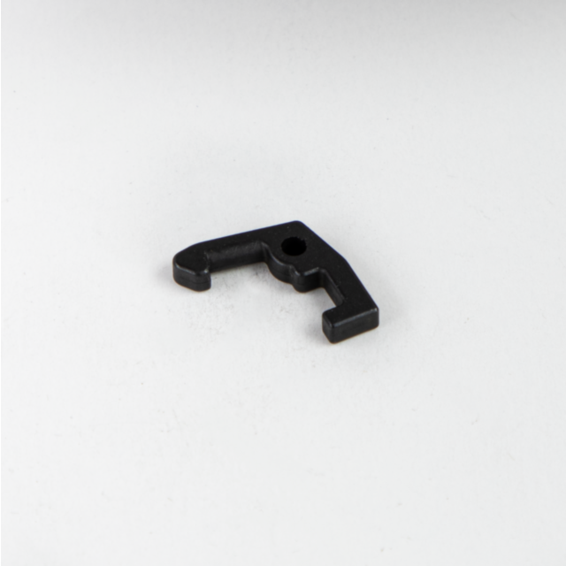 A small COCKING LEVER LATCH BREN 2, featuring a black metallic finish and an L-shaped design with a hole in the center, is placed on a plain white surface.
