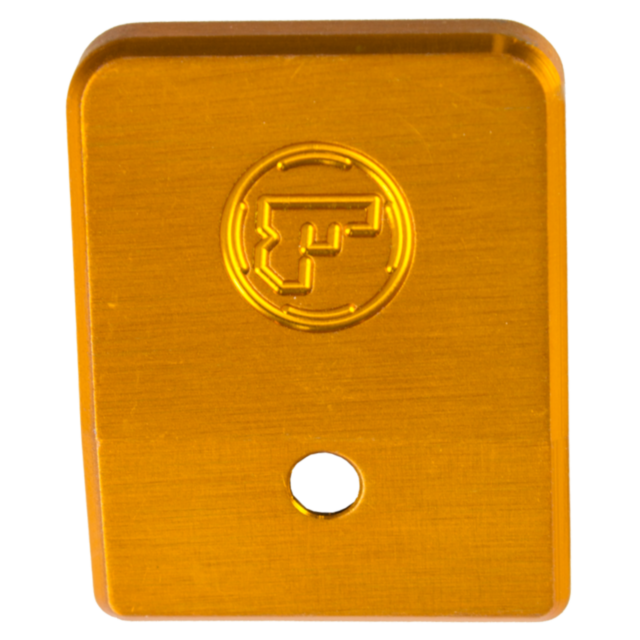 The ALUMINUM MAGAZINE BASE PAD TS ORANGE is a rectangular, gold-colored aluminum plate featuring an embossed "F" within a circle near the top and a circular hole situated near the bottom.
