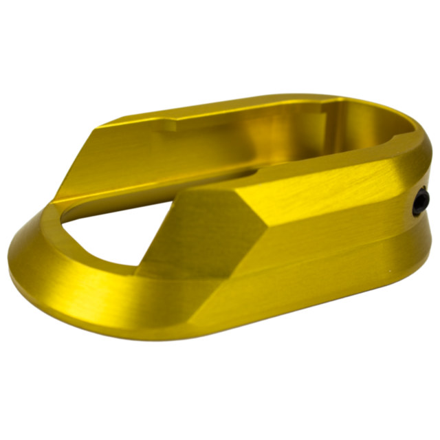 A gold metallic object with a smooth, curved surface and angular edges, resembling a component or part. It features an open center and is set against a plain white background, much like the ALUMINUM MAGWELL SHADOW 2 GOLD.