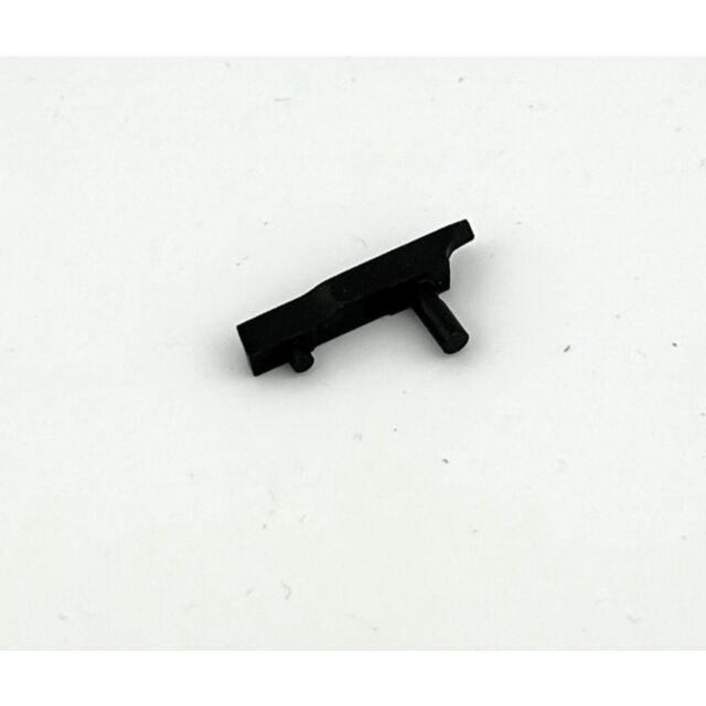 A DWX Ejector, a small black plastic object with a protruding peg and a rectangular shape, lies on a white surface.