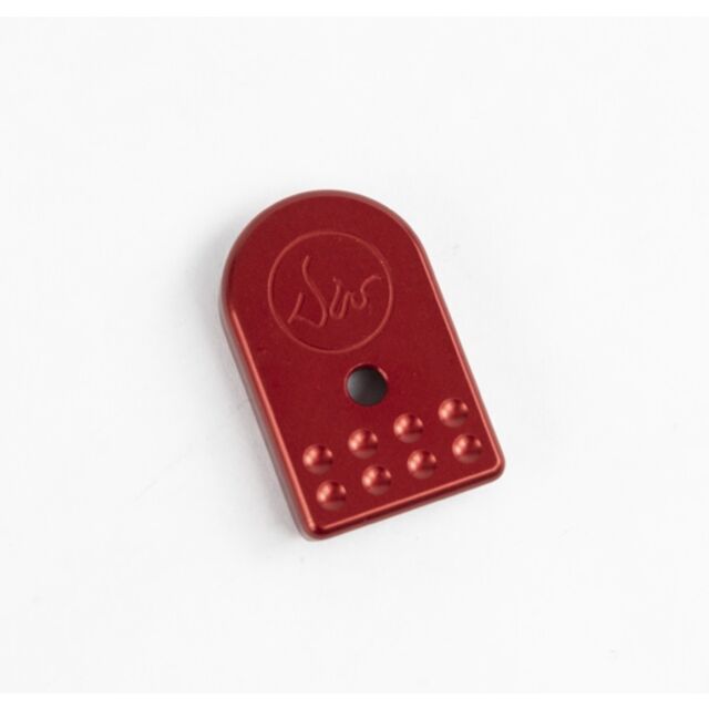 Product Name: DWX Magazine Base Pad Red - A compact, red, oval object with a center hole. It features embossed dots on the lower half and an abstract design on the upper, all set against a plain white background.