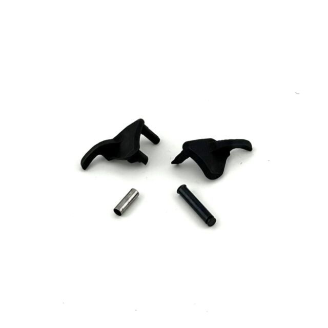 On a plain white background are two DWX Thumb Safety Compact Ambi Sleeves in black plastic, alongside two small metal cylindrical rods that vary slightly in color and size. The compact plastic pieces feature protruding edges that could function as connect