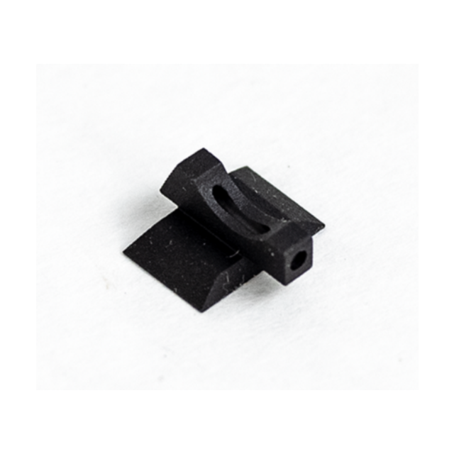 A "FRONT SIGHT FIBER OPTIC TARGET .140" in black plastic or metal, featuring a small rectangular base with an elongated hole in the center, is placed on a white surface. The design of the item is simple and geometric.