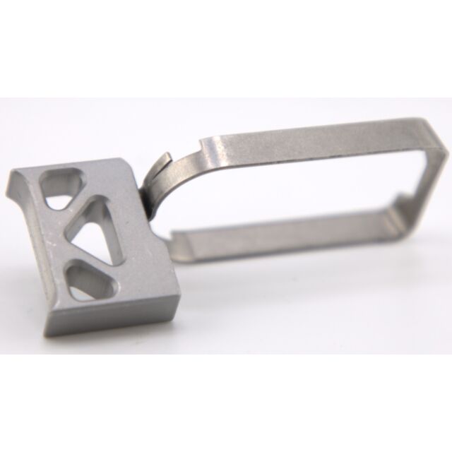 Close-up of the DWX COMPACT TRIGGER ASM, SILVER on a white background. This tool boasts a rectangular handle adorned with a perforated geometric design on one end for enhanced grip and a thin, curved metal rod forming a loop on the other end for ejecting